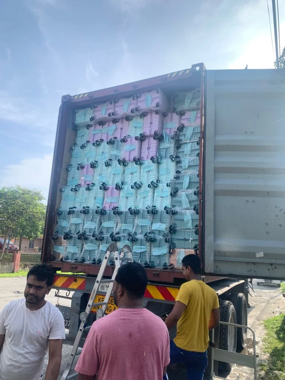 Three workers at the open door of a shipping container packed with wrapped pink and blue cases